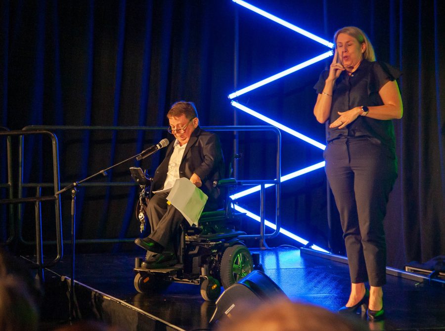 A man in a wheelchair giving a speech beside a deaf translator